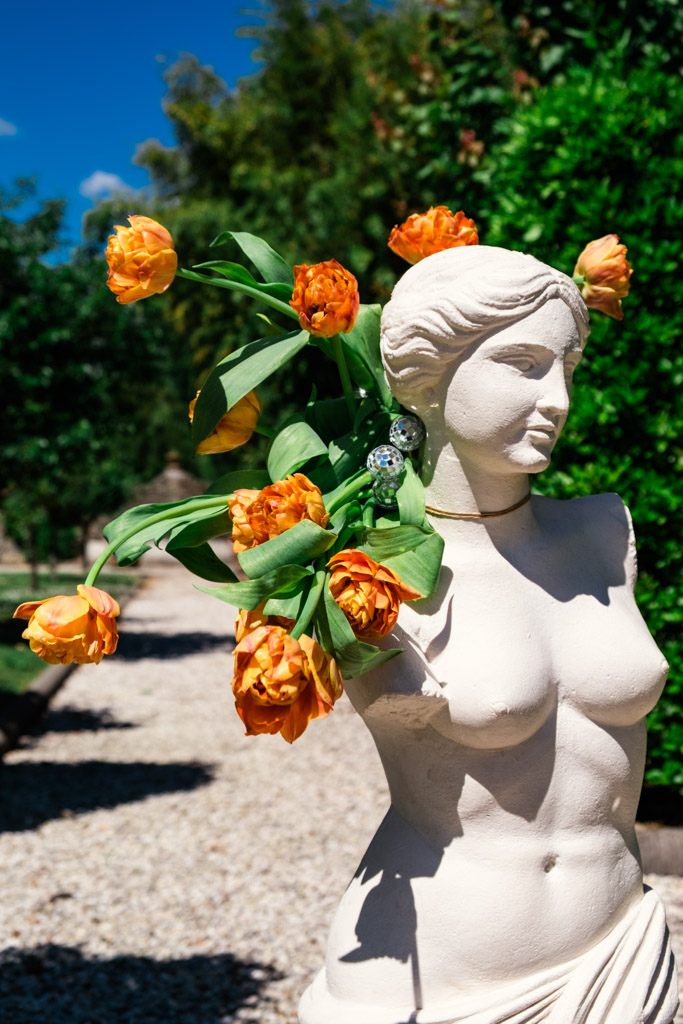 White statue with orange flowers arranged on its shoulders, outdoors in a sunny garden at Villa Moscheni in Tuscany, Italy
