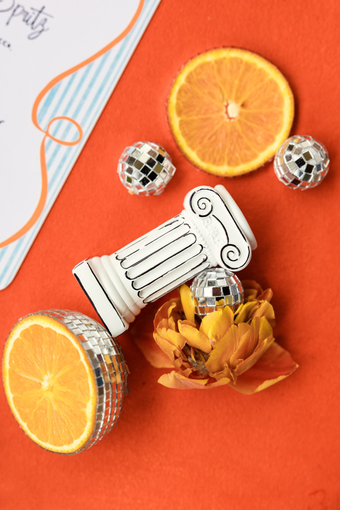 Mini column, disco balls, orange slices, and a yellow flower on an orange surface with a paper in the corner for wedding pool party at Villa Moscheni in Tuscany, Italy