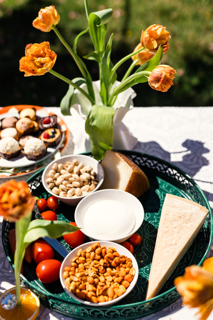 A tray with cheese, nuts, cherry tomatoes, and a vase of orange tulips sits on a sunny outdoor table for Italy wedding weekend celebration