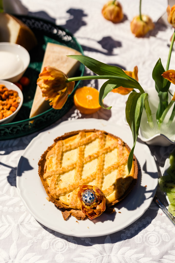 A lattice-top pie on a white plate sits among orange tulips and other food on a sunlit tablecloth for Italy destination wedding weekend