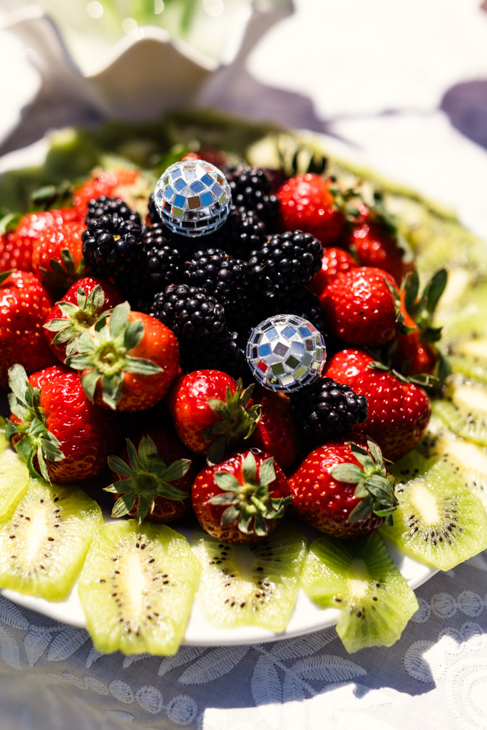 A plate of strawberries, blackberries, and kiwi slices with two small disco balls on top for Italy wedding weekend