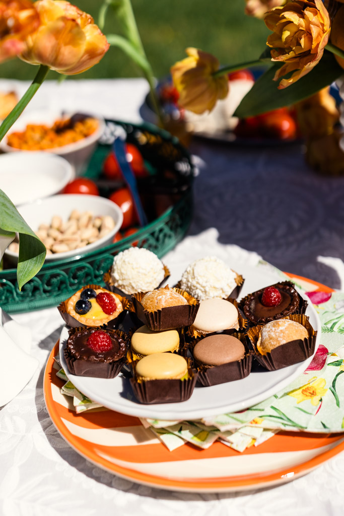 Assorted mini desserts on a plate with flowers and bowls of snacks on a table outdoors for Italy wedding celebration