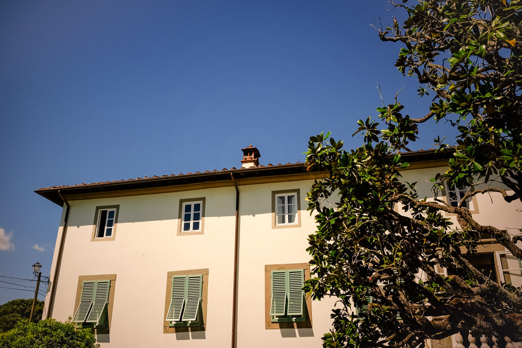 White villa with green shutters and a tree in front, set against a clear blue sky in Tuscany