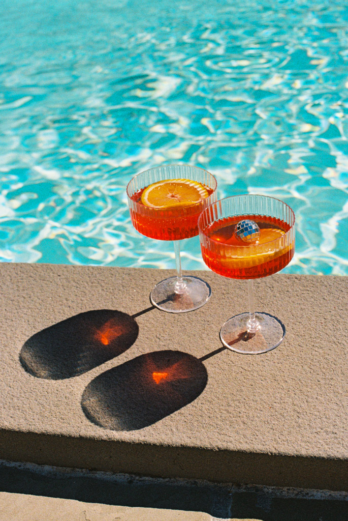 Film photo of two orange cocktails in crystal glasses by a swimming pool during wedding pool party at Villa Moscheni in Tuscany, Italy
