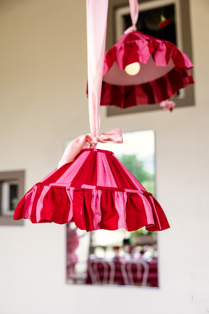 Red and pink ruffled lampshade hanging by a pink ribbon, reminiscent of a romantic Tuscany wedding, with a mirror in the background.