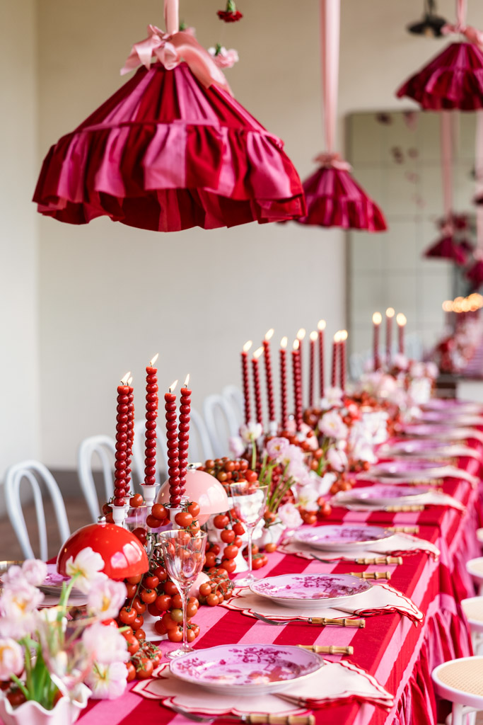 Long dining table with red decor, tall red candles, pink flowers, and red hanging lampshades above—perfect for an elegant Tuscany wedding.