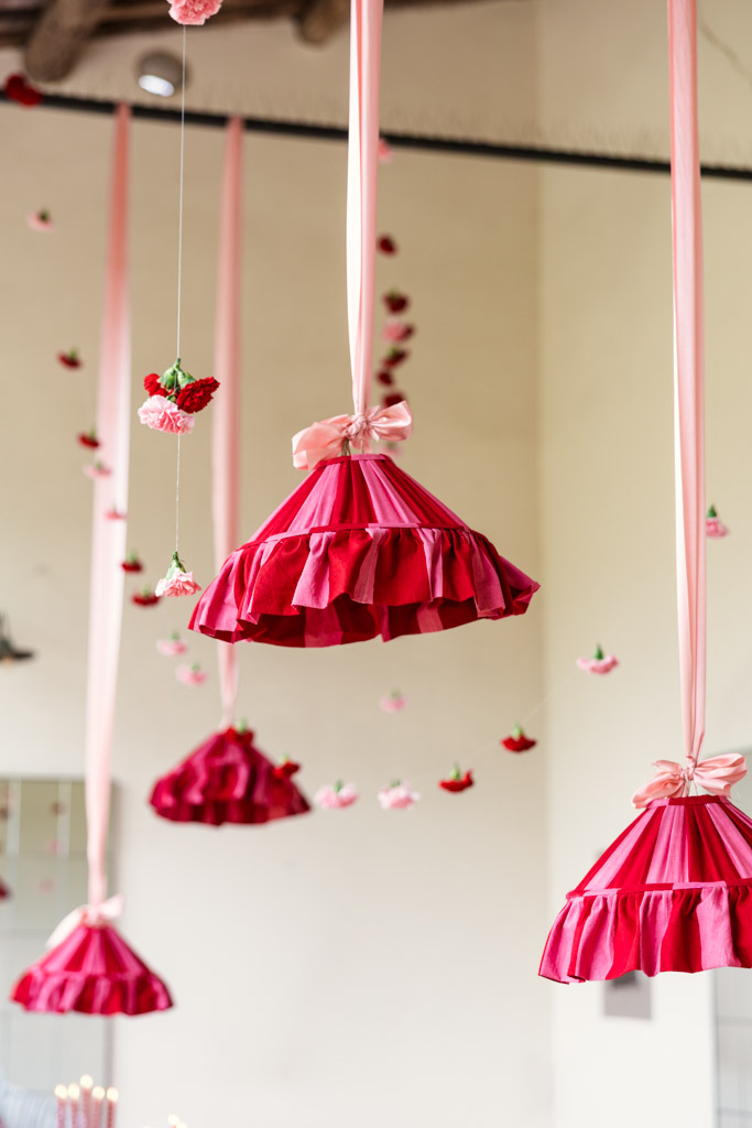 Pink, ruffled fabric lampshades hang from the ceiling with pink ribbons; small flowers float around them, evoking the romantic ambiance of a Tuscany wedding.