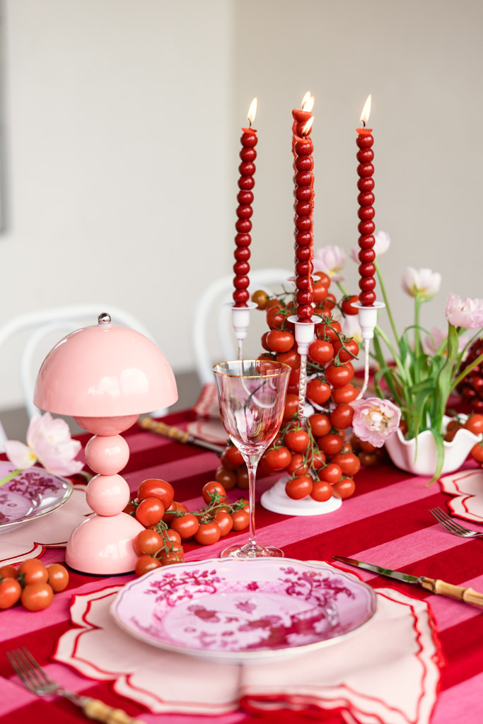 A red and pink table setting inspired by a Tuscany wedding, featuring ripe tomatoes, floral plates, a delicate pink lamp, and three red beaded candles.