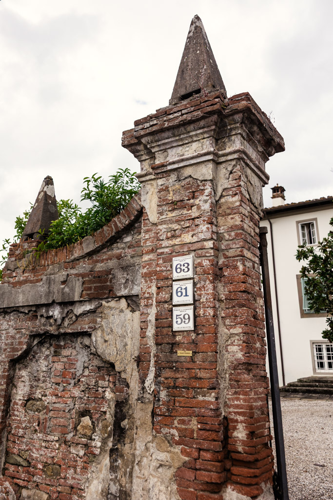 Weathered brick gatepost with three address numbers: 63, 61, and 59, in front of a white building—evoking the rustic charm of a Tuscany wedding.
