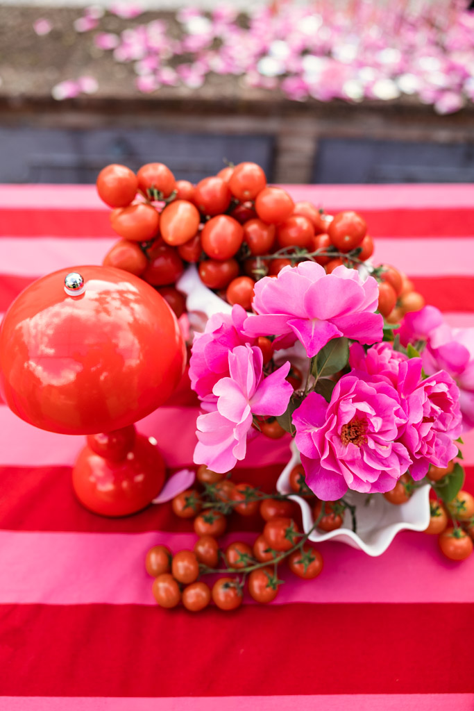 Red lamp, pink flowers, and cherry tomatoes arranged on a pink and red striped tablecloth evoke the vibrant charm of a Tuscany wedding.