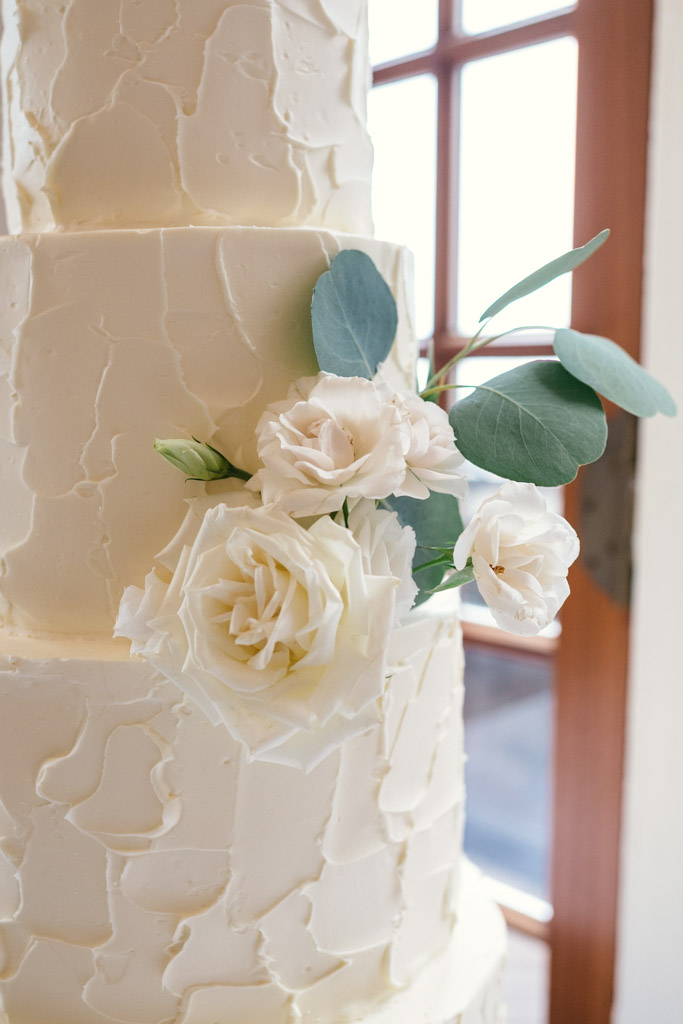 Multi-tiered white wedding cake with textured icing, decorated with white roses and green leaves for wedding celebration at the University Club of Chicago