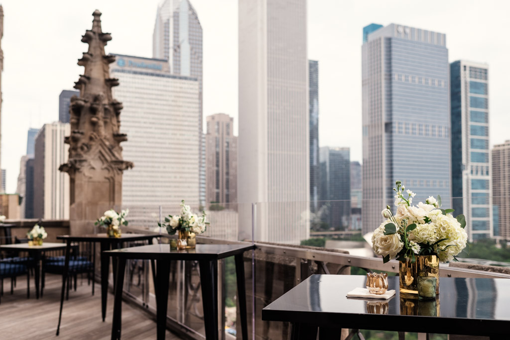 Outdoor balcony at the University Club of Chicago with black tables, floral centerpieces, and a city skyline in the background, decorated for wedding celebration