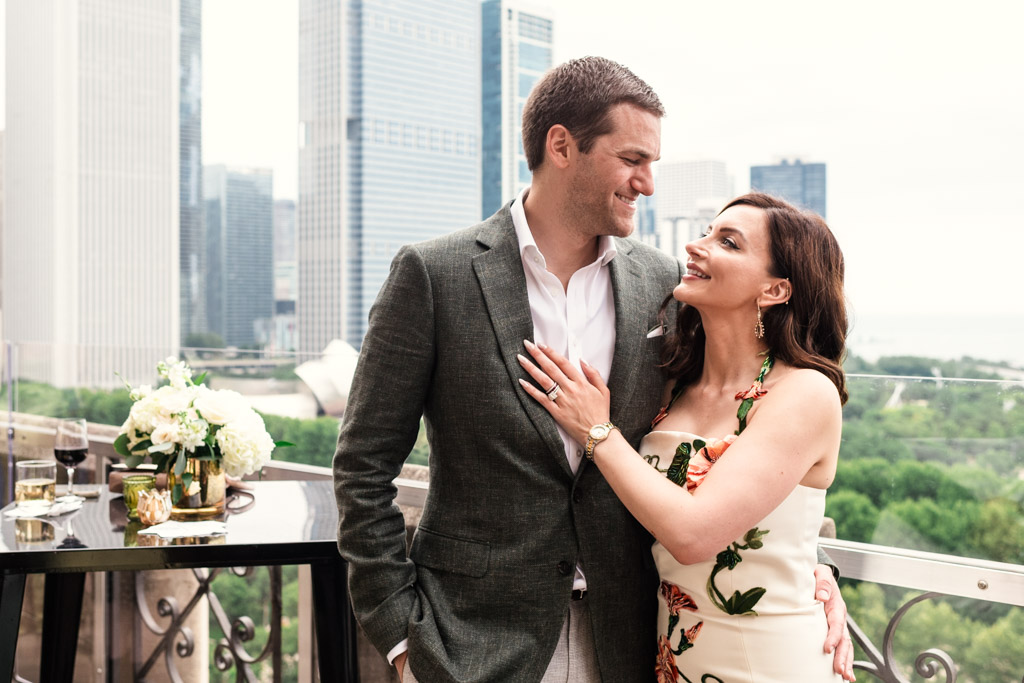 Newlywed couple smiles at each other on a balcony of the University Club of Chicago, with city buildings and greenery in the background