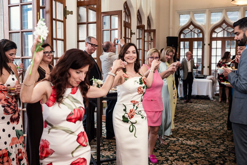 Bride and guests in floral dresses dance in a line during wedding celebration at the University Club of Chicago