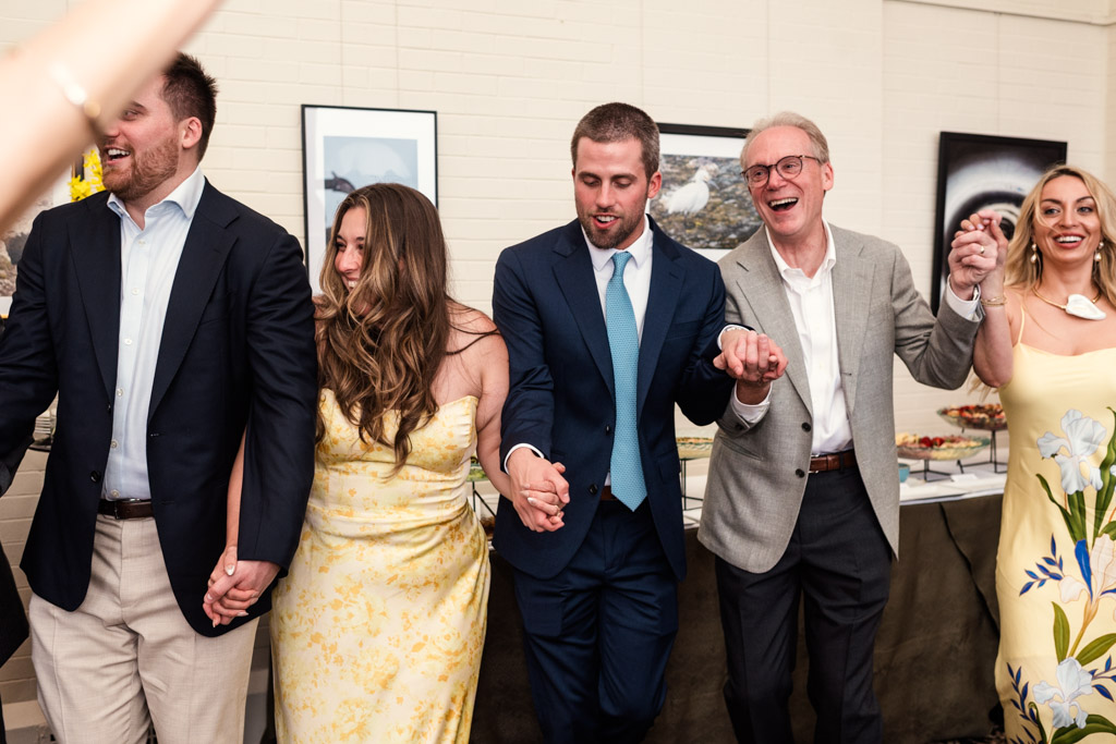 Guests dressed formally stand in a row, holding hands and smiling during a wedding celebration at the University Club of Chicago