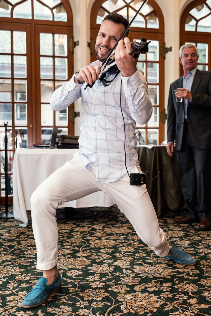 A man energetically plays a violin indoors during wedding celebration at the University Club of Chicago