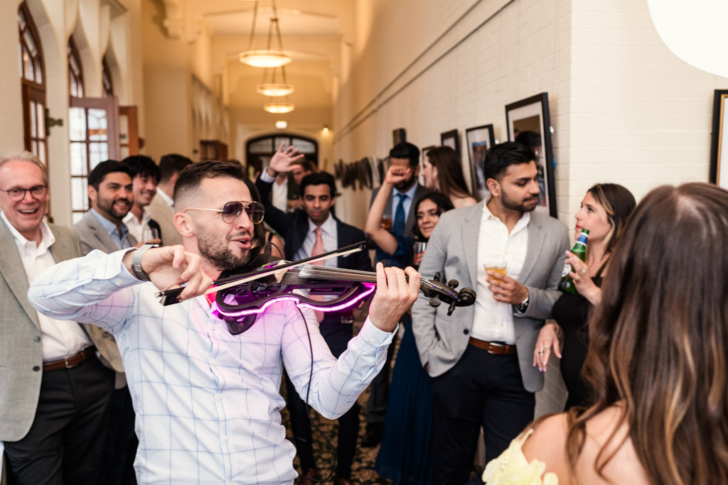 Man playing electric violin with pink lights at University Club of Chicago wedding celebration surrounded by guests