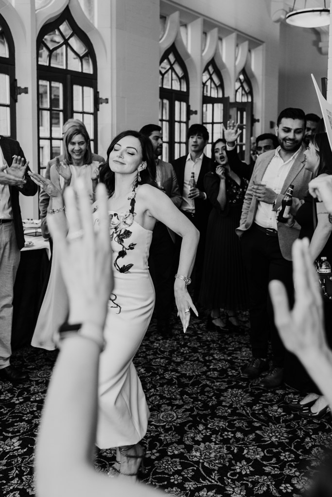 Bride dances joyfully in a crowdduring wedding celebration at the University Club of Chicago, with people clapping and smiling around her