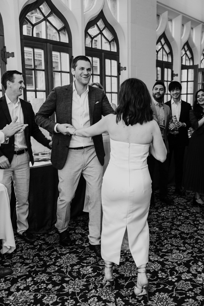 Black and white photo of bride and groom dancing together in a room full of smiling, well-dressed guests during their wedding celebration at the University Club of Chicago