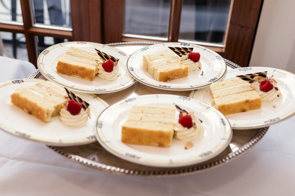 Five plates with slices of layered cake, whipped cream, raspberries, and chocolate arranged on a silver tray for wedding celebration at University Club of Chicago