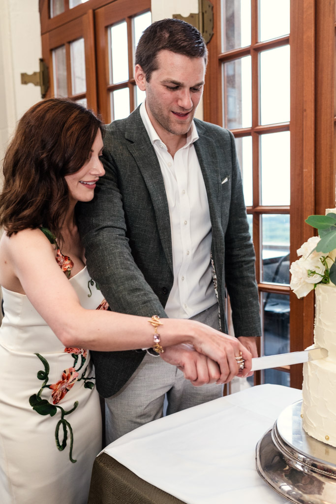 Newlywed couple smiles as they cut a white tiered cake togetherduring wedding celebration at the University Club of Chicago