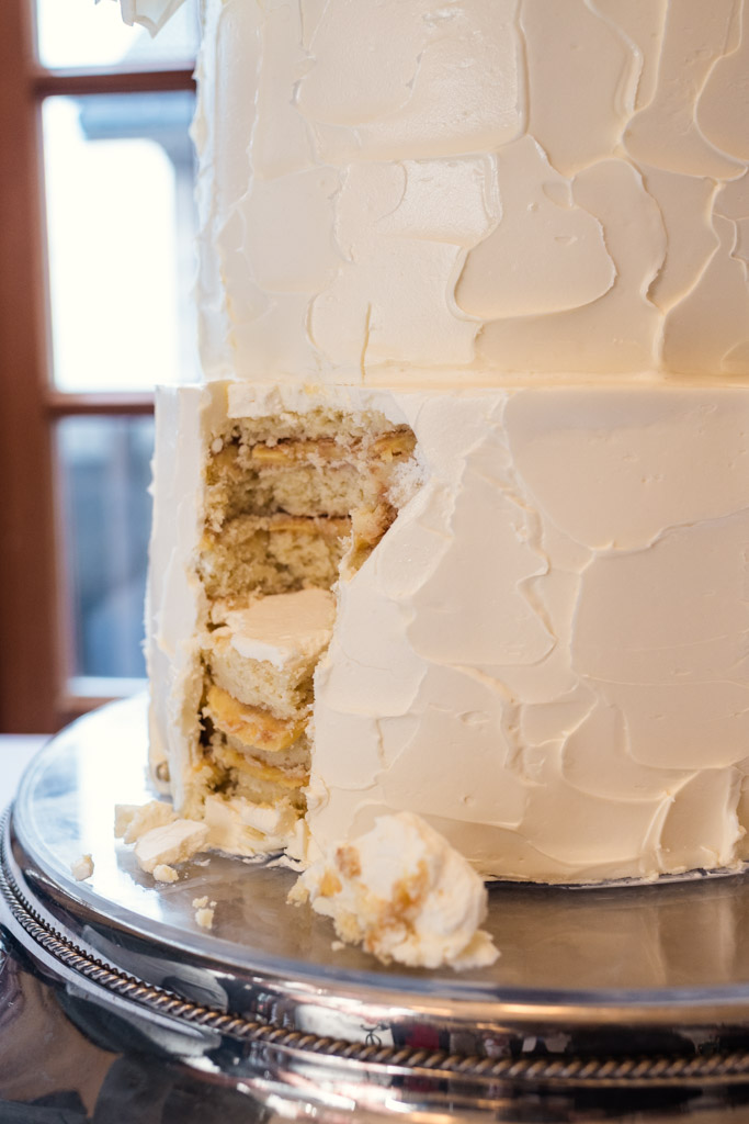 Detail photo of a white frosted wedding cake, served at the University Club of Chicago, with a large slice missing from the bottom tier