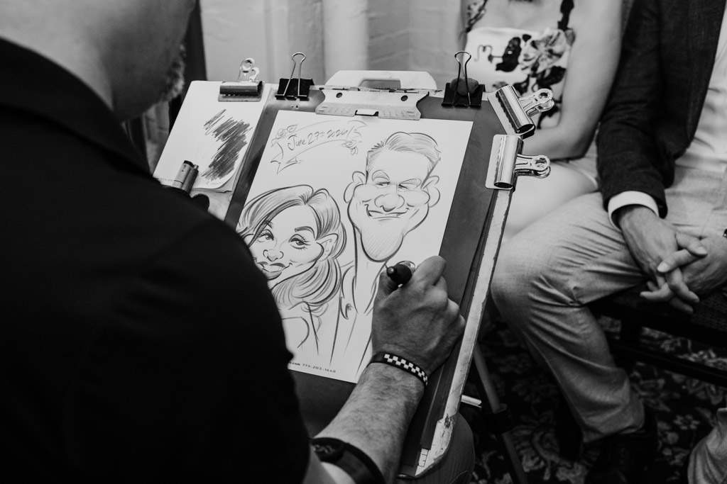 Black and white photo of artist drawing a caricature of newlywed couple seated in front of him during University Club of Chicago wedding celebration