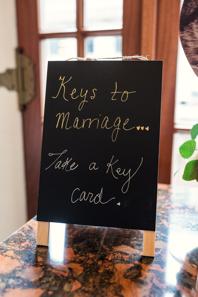Small blackboard sign says: “Keys to Marriage... Take a key card.” on a marble countertop for wedding celebration at the University Club of Chicago