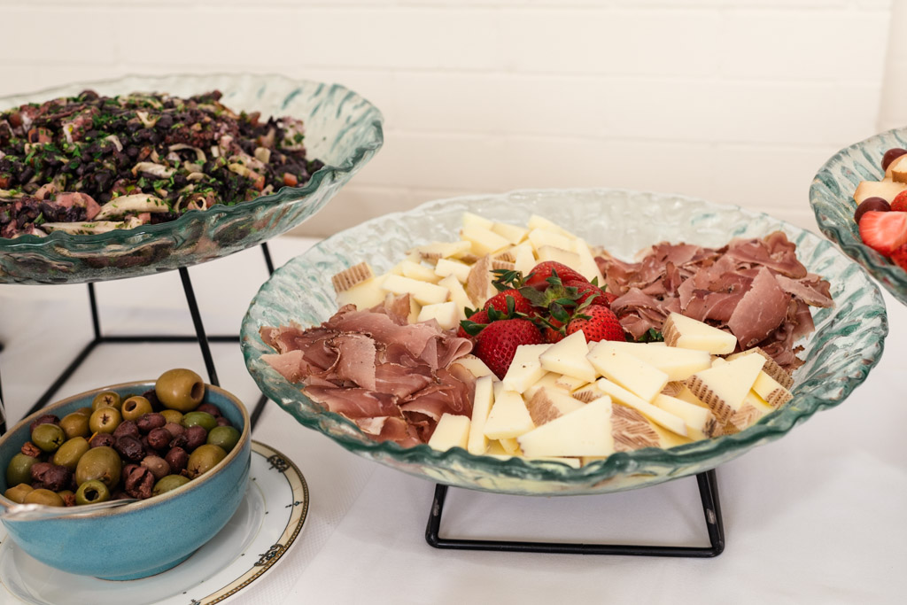 A platter with sliced cheese, cured meats, and strawberries, next to bowls of olives and a bean salad for wedding celebration at the University Club of Chicago