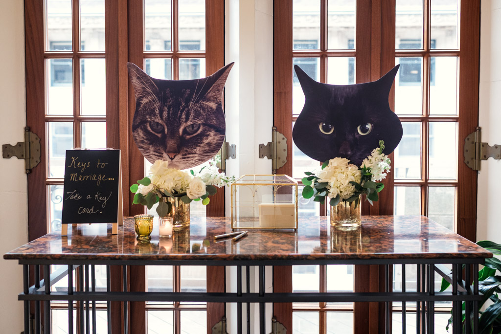 Table with flowers, candles, a card box, a sign, and two large cat face cutouts for wedding celebration at the University Club of Chicago