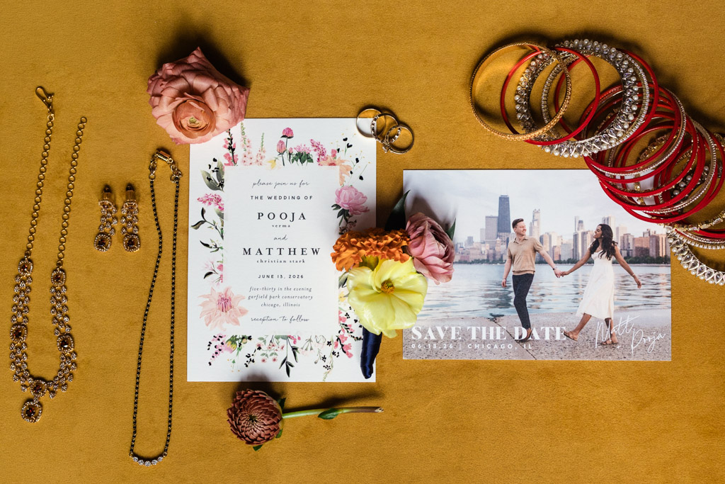 Wedding invitation, save-the-date card, jewelry, bangles, and flowers arranged on a gold surface for Chicago Indian wedding at Garfield Park Conservatory
