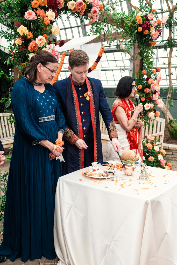 A man and a woman in formal attire stand by a decorated table at a festive indoor ceremony, celebrating a vibrant Chicago Indian wedding.