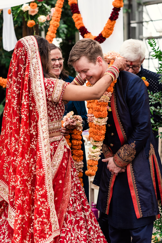 Bride puts a flower garland on groom during a colorful Chicago Indian wedding ceremony with guests smiling.