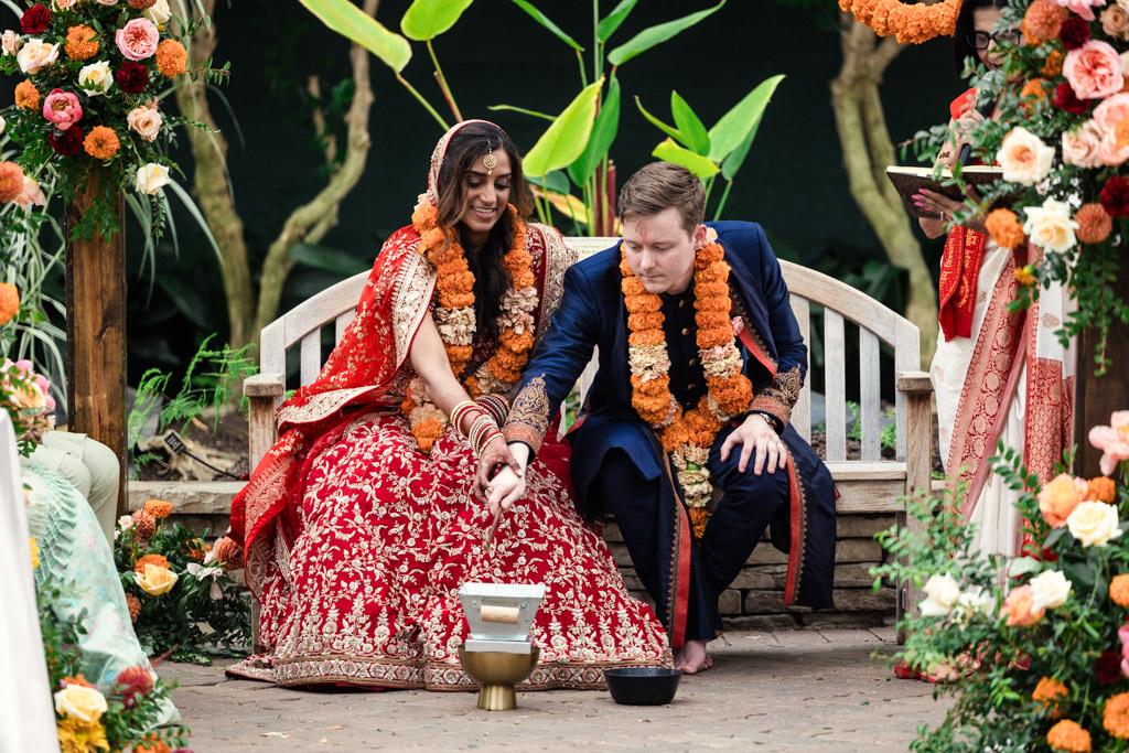 A bride and groom in traditional attire sit together, performing a ritual during their Chicago Indian wedding ceremony.