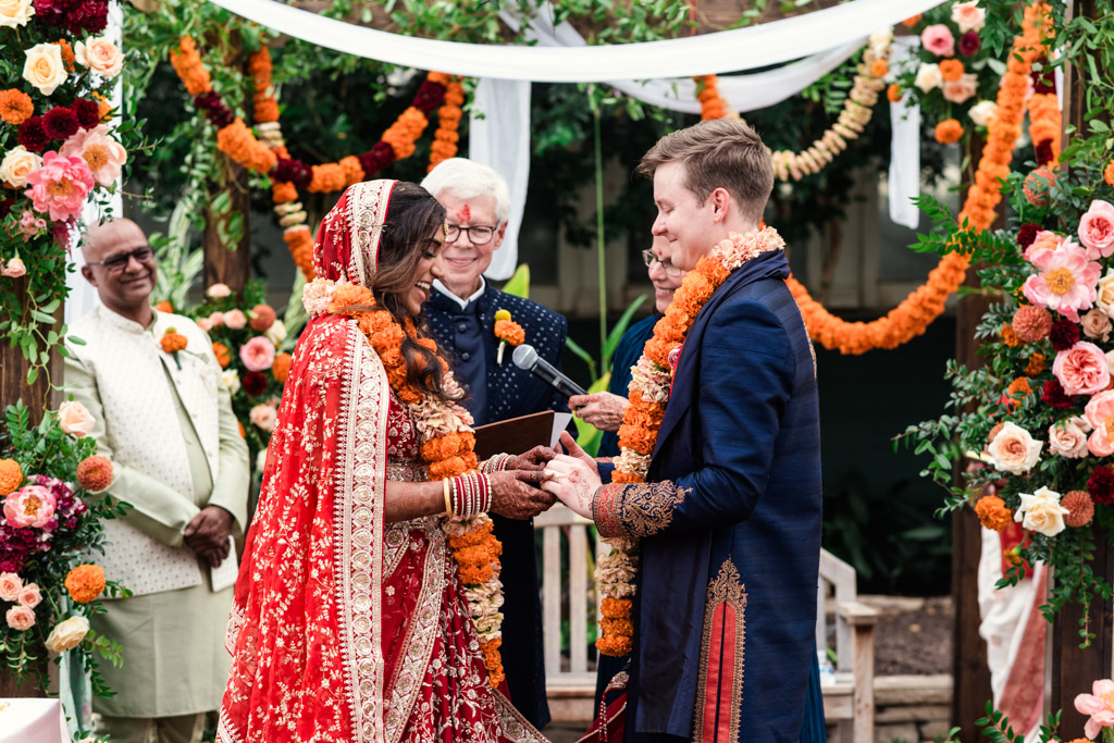 A bride and groom exchange vows at a vibrant Garfield Park Conservatory Indian wedding ceremony, beautifully decorated with flowers and orange garlands