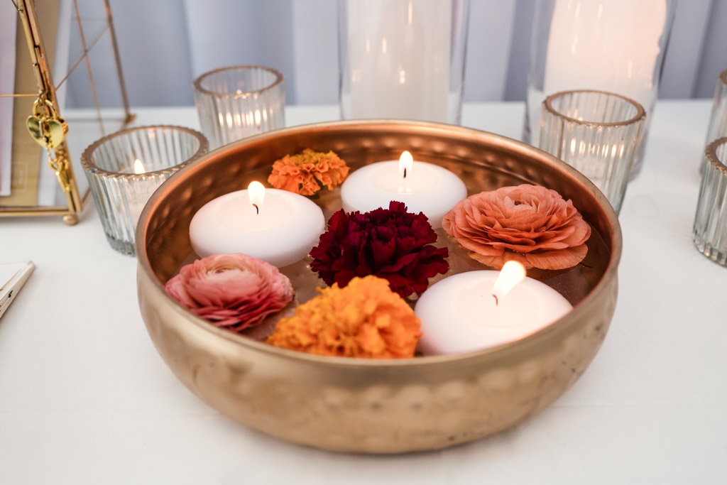 Gold bowl with floating candles and colorful flowers, surrounded by glass candle holders on a white surface for Chicago Indian wedding at Garfield Park Conservatory