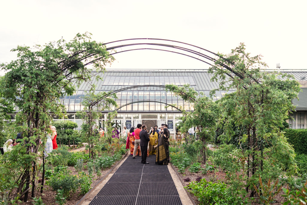 Exterior of Garfield Park Conservatory wedding reception space with guests on a garden path under metal arches