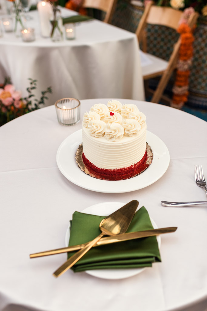 Small white cake with red trim on a table, next to a green napkin and gold cake serving utensils for wedding celebration at Garfield Park Conservatory