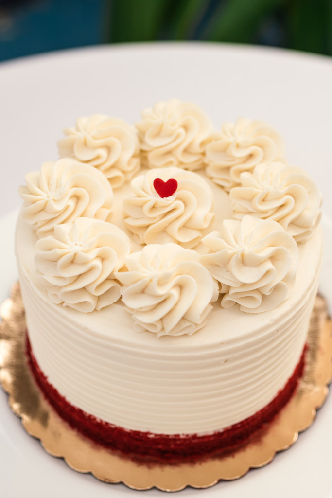White frosted cake with swirls of icing and a small red heart on top, on a gold cake board for Chicago Indian wedding reception at Garfield Park Conservatory
