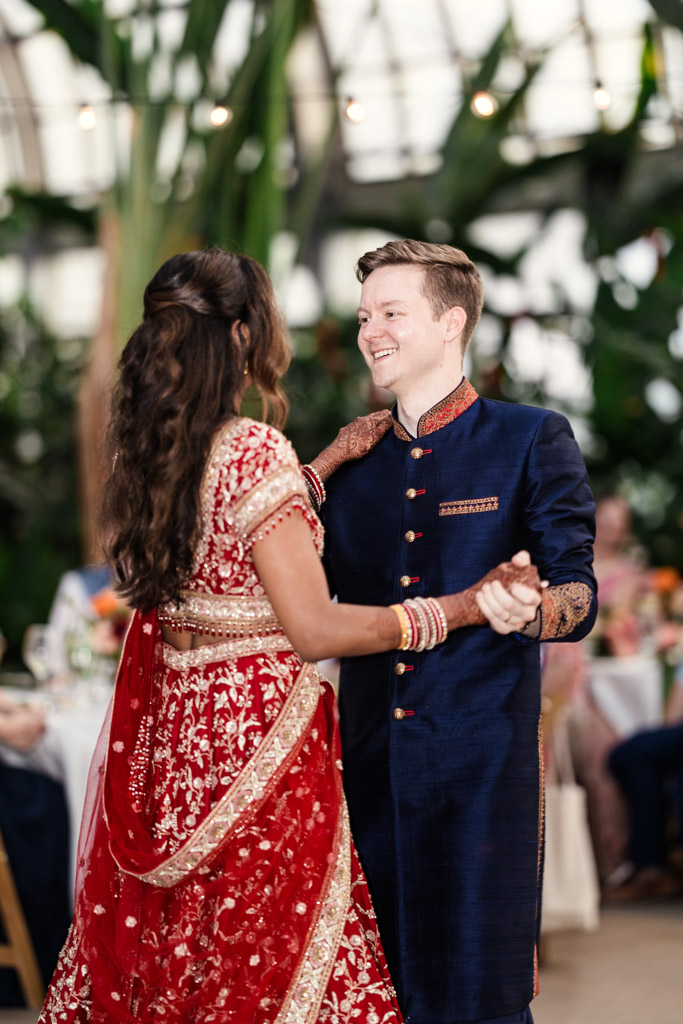 Newlywed couple in traditional attire dances together at their Garfield Park Conservatory Indian wedding reception, with greenery in the background