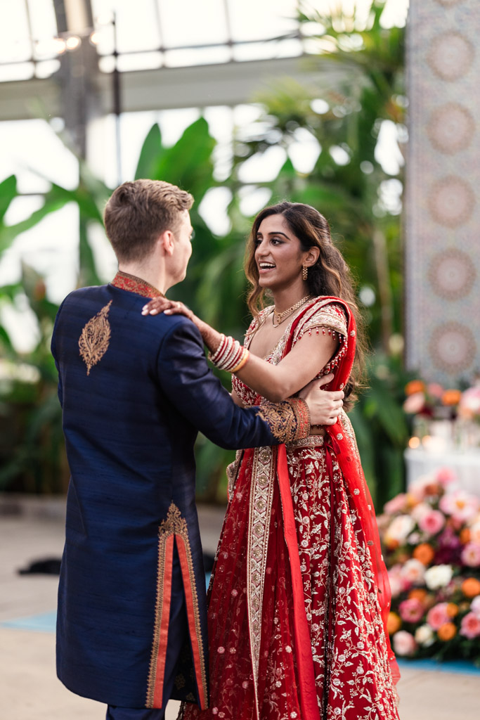 Newlyweds in traditional attire dance together, smiling, at their indoor Chicago Indian wedding reception adorned with elegant floral decorations