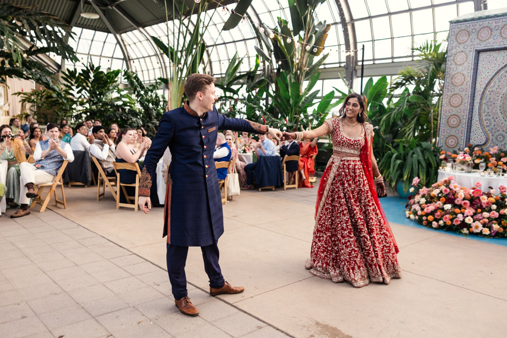 Bride and groom in traditional attire dance during their Garfield Park Conservatory wedding reception as guests watch and smile