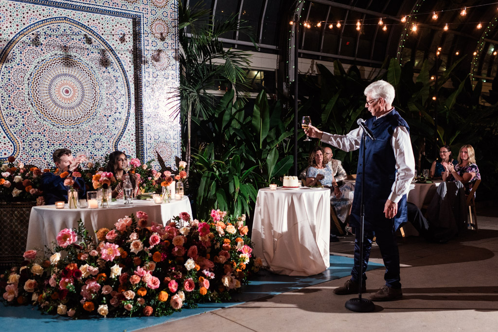 Groom's father gives a toast during Garfield Park Conservatory wedding reception amid beautiful flowers, glowing candles, and guests seated at decorated tables