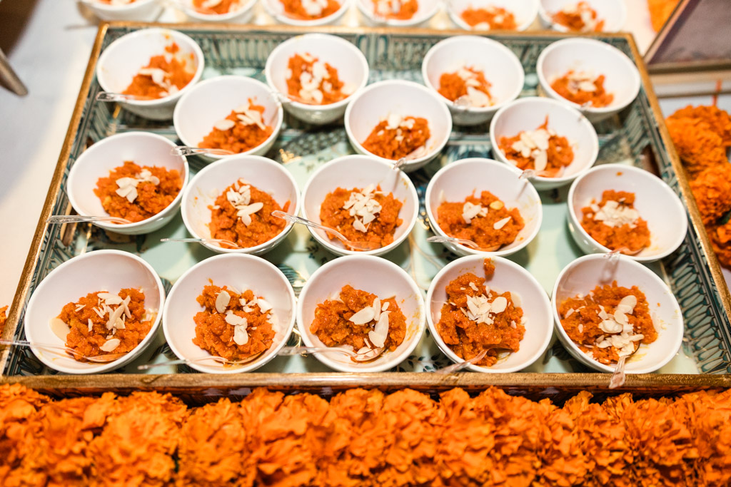 Small white bowls of orange dessert topped with almond slivers, arranged on a tray with vibrant orange flowers for Chicago Indian wedding reception