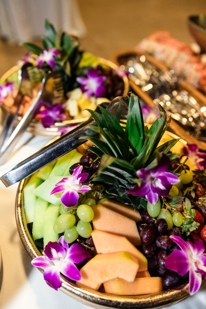 Bowls of fresh fruit, including melon and grapes, garnished with purple orchids and metal tongs for wedding reception at Garfield Park Conservatory
