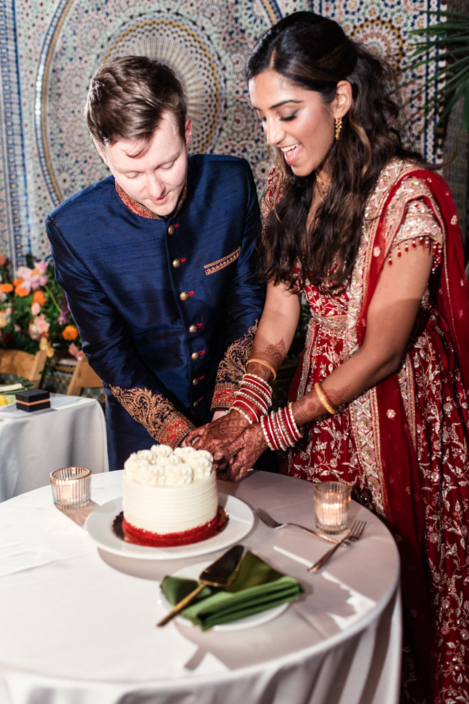 Newlyweds in traditional Indian attire cut a white cake together during their Chicago Indian wedding celebration