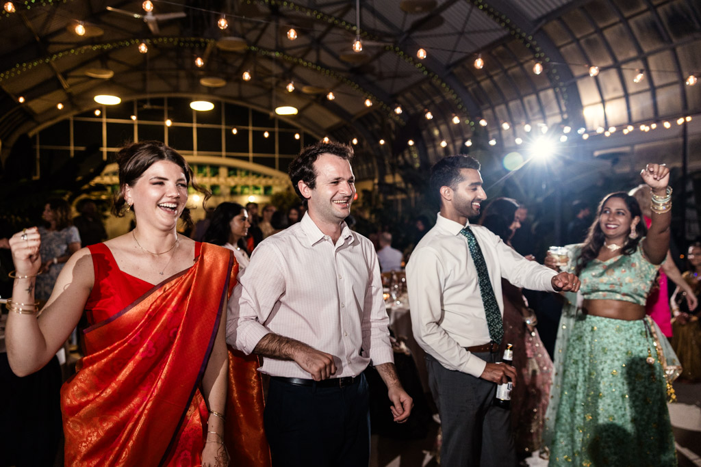 Four guests dance and smile during wedding reception at Garfield Park Conservatory with string lights overhead