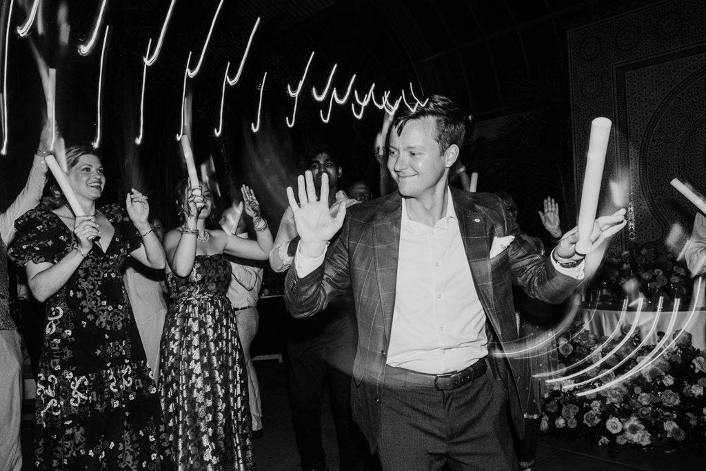 Creative black and white photo of groom and guests dancing with glowsticks during Indian wedding reception at Garfield Park Conservatory