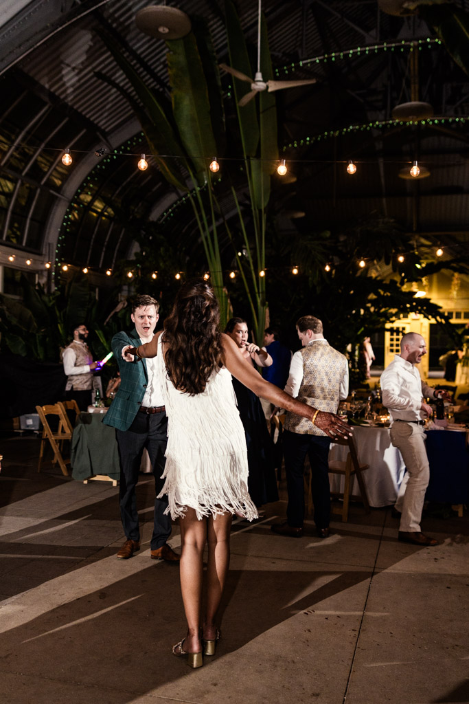 Bride in a fringed white dress dances with groom during their wedding reception at Garfield Park Conservatory