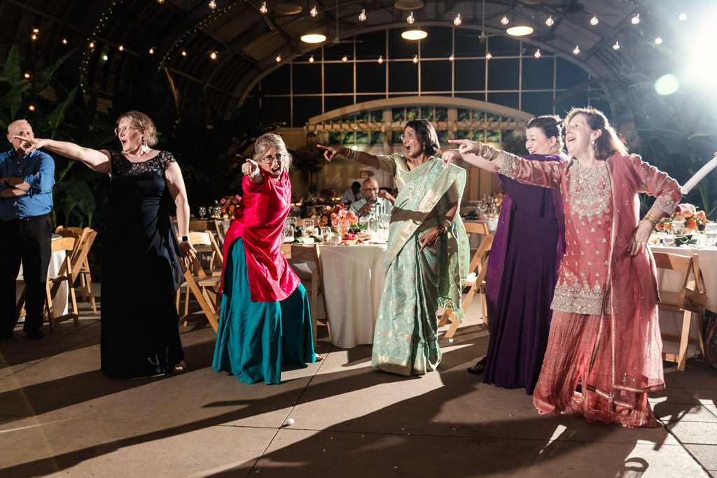 Five women in colorful dresses dance and point during Chicago Indian Wedding at Garfield Park Conservatory